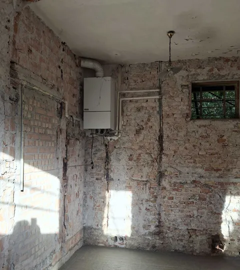 Stanza in restauro con muri in mattoni a vista e una vecchia caldaia murale